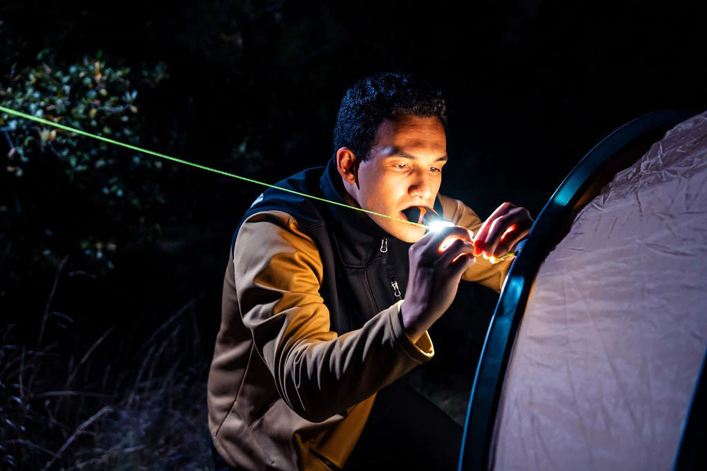 illumibite hands-free flashlight held in mouth using bite grip while setting up a tent in low-light outdoor conditions